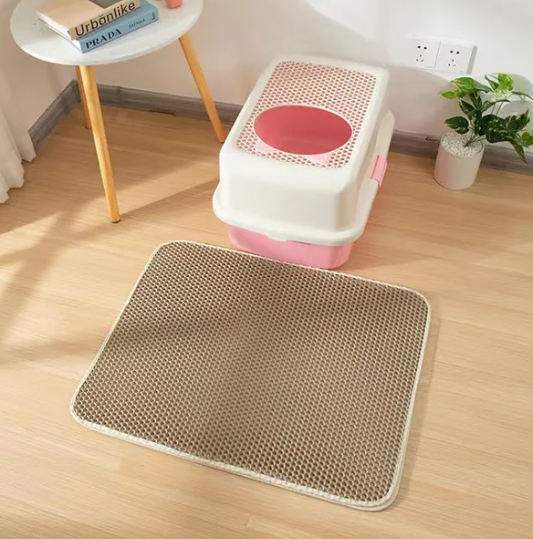 khaki brown cat litter mat/pad and a litter box and a background of a room with a wooden floor, round table and a plant